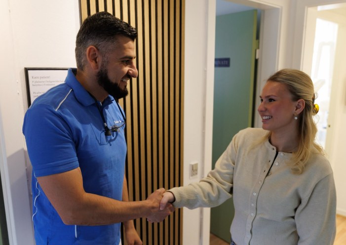 Tandlægen giver hånd til en patient ved klinikkens trævæg